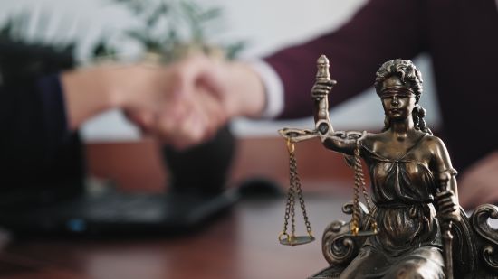 Lady Justice statue with two people shaking hands in the background, symbolizing Gloria Estefan legal settlement.