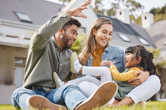 Family sitting on the lawn of their new home, smiling together.