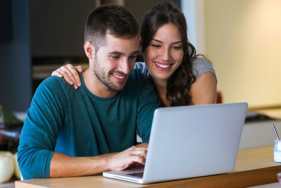 Smiling couple using a laptop, researching how to sell a structured settlement online for financial solutions.