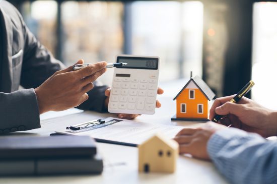 Professionals discussing home financing with a calculator and house models.