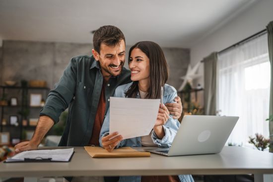 Couple celebrating financial progress at home, holding paperwork related to selling a structured settlement.