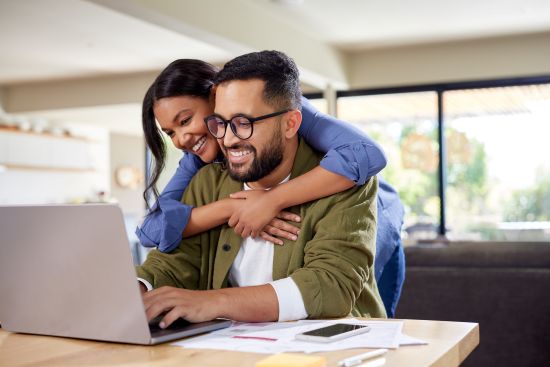 A smiling couple working on a laptop, researching options to sell their annuity for fast cash at home.