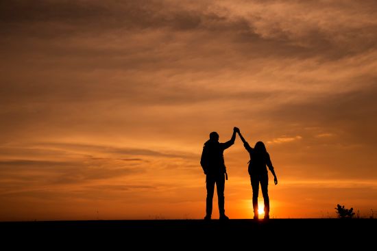 Silhouette of two people holding hands at sunset, symbolizing financial empowerment.